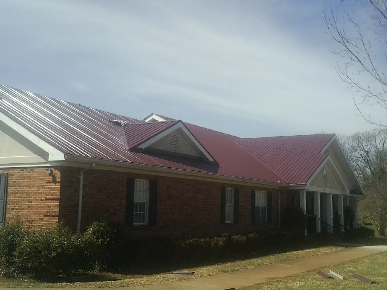 Red metal roof with gabled entries on a long brick building, from a Hail Damage Roof Repair job in Ulster Park