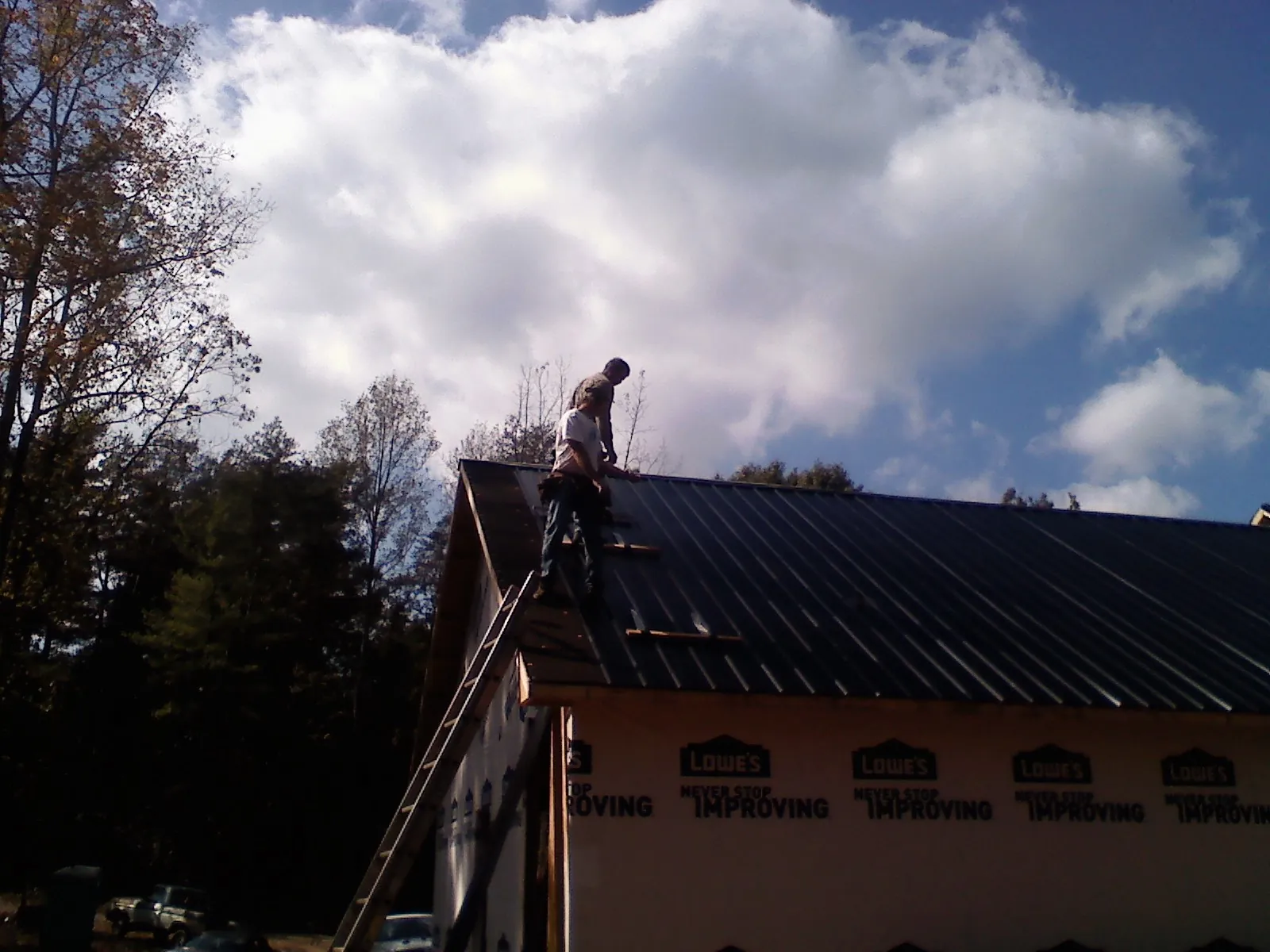 Roofer fastening dark metal panels high against a cloudy sky, from a Roof Inspection job in Ulster Park