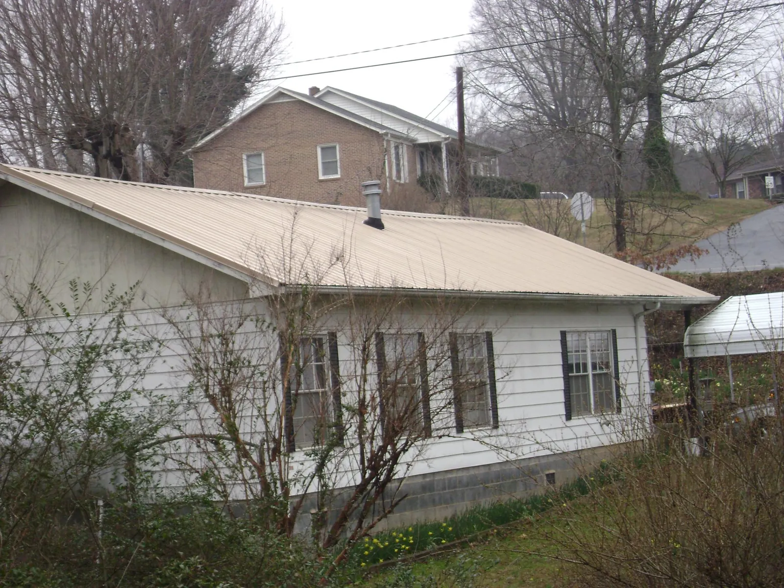Tan metal roof on a white sided house set into a hillside — Commercial Roofing by Roofing Brothers in Ulster Park